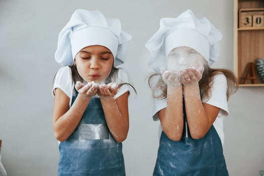 Two little girls in blue chef uniform blows the flour out of hands on the kitchen photo
