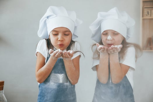 Two little girls in blue chef uniform blows the flour out of hands on the kitchen photo