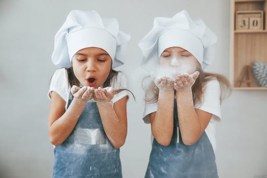 Two little girls in blue chef uniform blows the flour out of hands on the kitchen photo