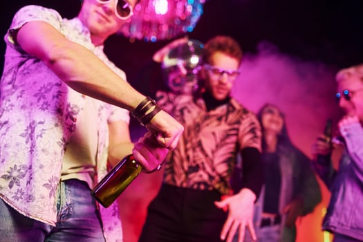 Celebrating and knocking bottles with alcohol. Young people is having fun in night club with colorful laser lights photo