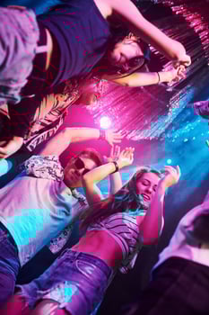 View from below of young people that having fun in night club with colorful laser lights photo