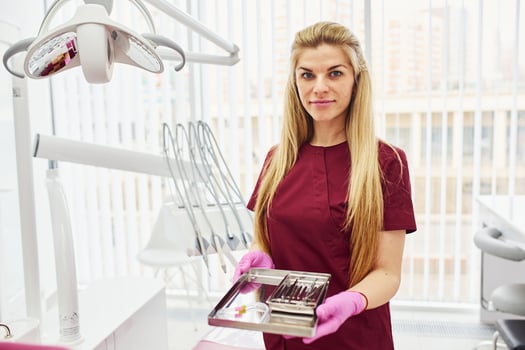 Young female dentist in uniform standing in stomatology office with tools in hands photo