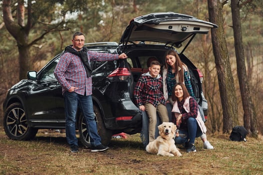 Happy family have fun with their dog near modern car outdoors in forest photo
