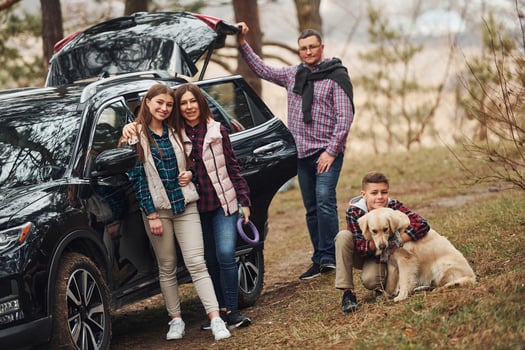 Happy family have fun with their dog near modern car outdoors in forest photo