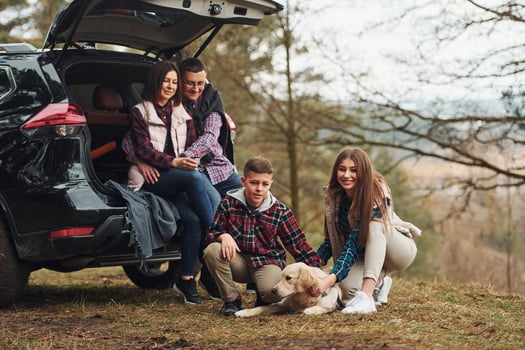Happy family sitting and having fun with their dog near modern car outdoors in forest photo