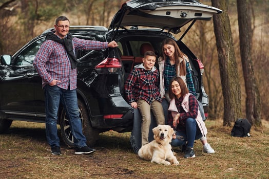 Happy family have fun with their dog near modern car outdoors in forest photo