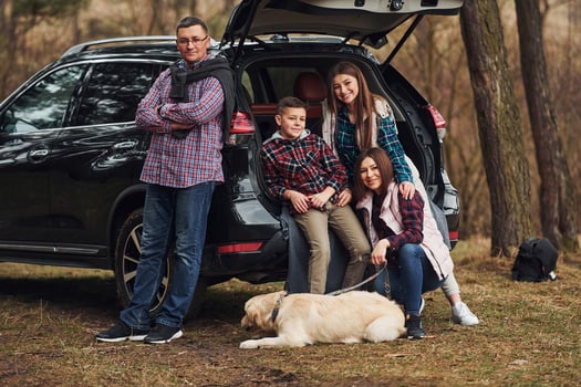 Happy family have fun with their dog near modern car outdoors in forest photo