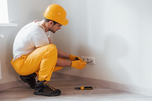 Handyman in yellow uniform works with electricity and installing new socket. House renovation conception photo