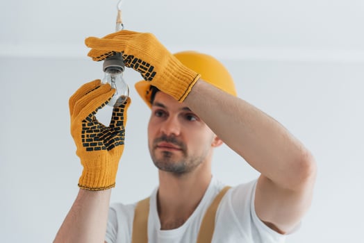 Handyman in yellow uniform changing light bulb. House renovation conception photo