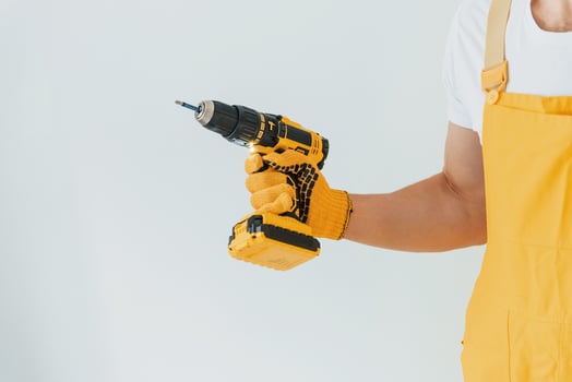Handyman in yellow uniform standing against white wall with automatic screwdriver. House renovation conception photo