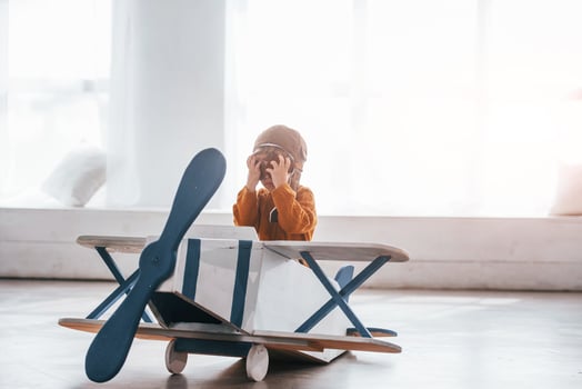 Little boy in retro pilot uniform having fun with toy plane indoors photo