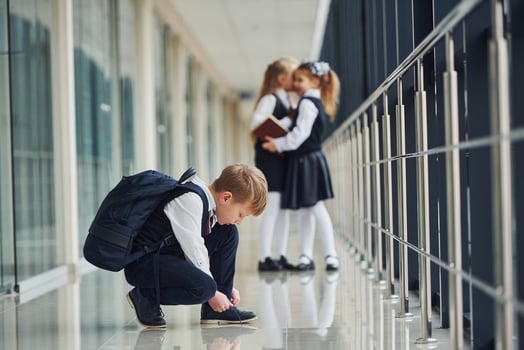 Boy sitting on the floor. School kids in uniform together in corridor photo