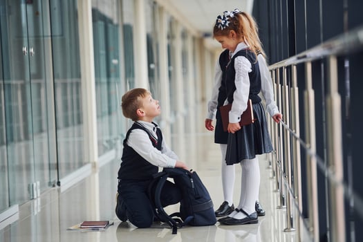 Boy sitting on the floor. School kids in uniform together in corridor photo