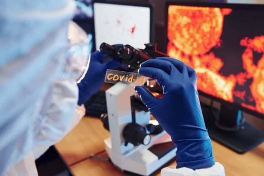 Scientist in white protective wear indoors in laboratory with lens with COVID-19 title on it photo