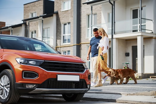 Going out from the building. Lovely couple have a walk together with dog outdoors near the car photo