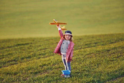 Cute little girl have fun with toy plane on the beautiful green field at sunny daytime photo
