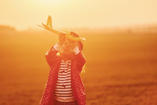 Illuminated by orange colored sunlight. Cute little girl have fun with toy plane on the beautiful field at daytime photo