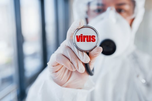 Nurse in white protective wear standing indoors with stethoscope with virus letter on it photo