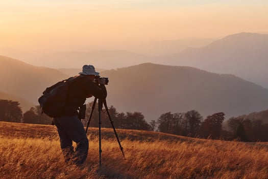 Male photographer standing and working at majestic landscape of autumn trees and mountains by the horizon photo