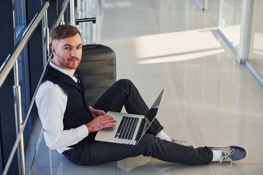 Young male passenger in elegant formal clothes sitting with laptop in the airport hall photo