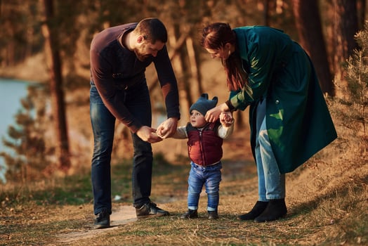 Mother and father with their little son have a walk in spring forest at daytime photo