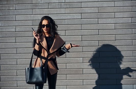 Beautiful brunette with curly hair and in black clothes talking by phone outdoors near wall photo