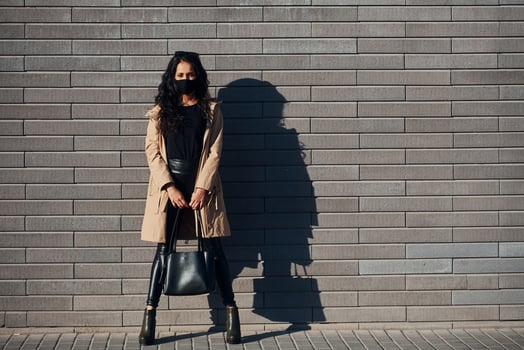 In protective mask. Beautiful brunette with curly hair and in black clothes outdoors near wall photo
