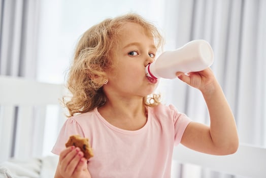 Having a breakfast by eating cookies. Cute little girl in casual clothes is indoors at home at daytime photo