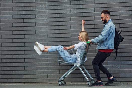 Having fun and riding shopping cart. Young stylish man with woman in casual clothes outdoors together. Conception of friendship or relationships photo