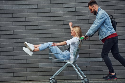 Having fun and riding shopping cart. Young stylish man with woman in casual clothes outdoors together. Conception of friendship or relationships photo