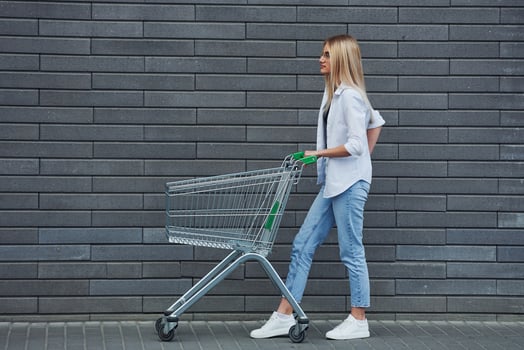 Beautiful blonde in casual clothes with shopping cart is outdoors at sunny daytime photo
