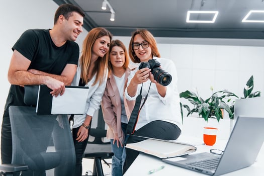 Group of business people in formal clothes indoors in the office looking at photos on the camera
