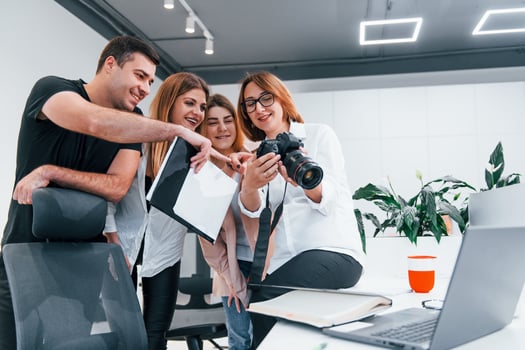 Group of business people in formal clothes indoors in the office looking at photos on the camera
