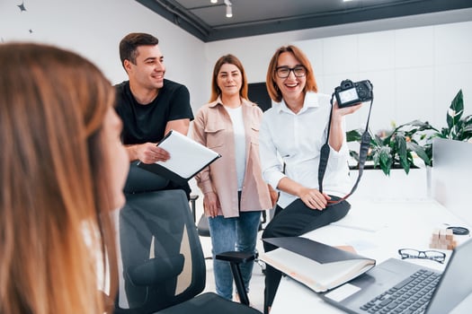 Group of business people in formal clothes indoors in the office looking at photos on the camera