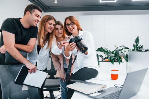 Group of business people in formal clothes indoors in the office looking at photos on the camera