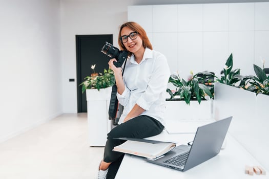 Woman in formal clothes and with camera sitting in the office photo