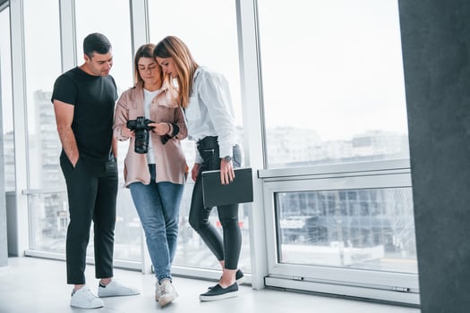 Group of people standing indoors together and looks at photos on camera
