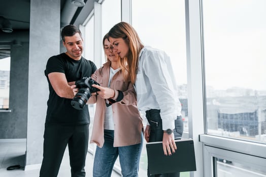 Group of people standing indoors together and looks at photos on camera