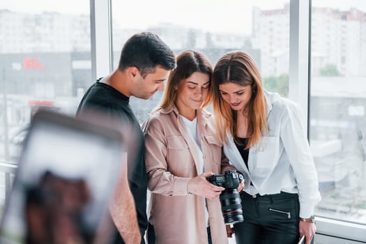 Group of people standing indoors together and looks at photos on camera