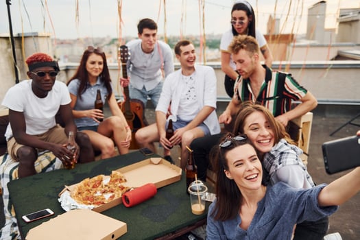 Girl making selfie. With delicious pizza. Group of young people in casual clothes have a party at rooftop together at daytime photo