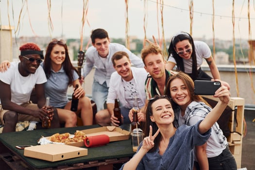 Girl making selfie. With delicious pizza. Group of young people in casual clothes have a party at rooftop together at daytime photo