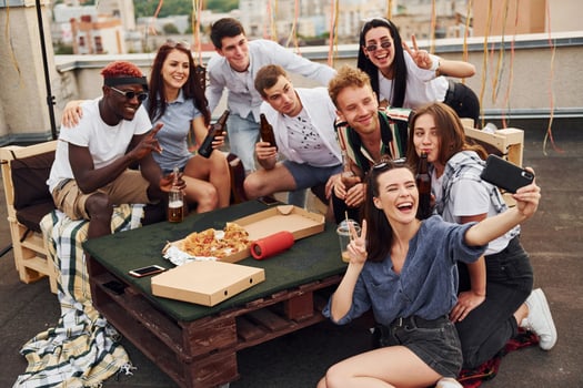 Girl making selfie. With delicious pizza. Group of young people in casual clothes have a party at rooftop together at daytime photo