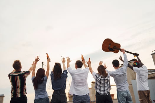 Standing high and looking at the cloudy sky. Group of young people in casual clothes have a party at rooftop together at daytime photo