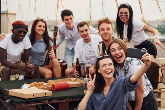 Girl making selfie. With delicious pizza. Group of young people in casual clothes have a party at rooftop together at daytime photo