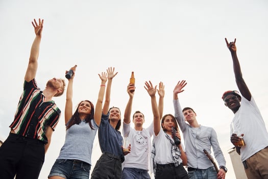 Standing high and looking at the cloudy sky. Group of young people in casual clothes have a party at rooftop together at daytime photo