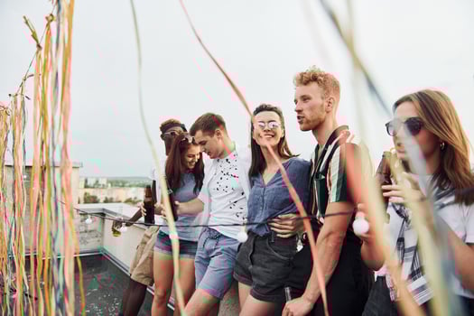 Leaning on the edge of the rooftop with decorates. Group of young people in casual clothes have a party together at daytime photo