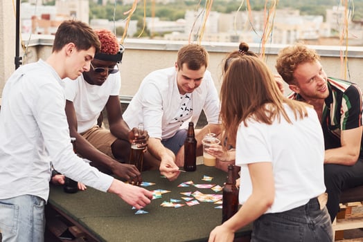 Playing game and sitting by the table. Group of young people in casual clothes have a party at rooftop together at daytime photo