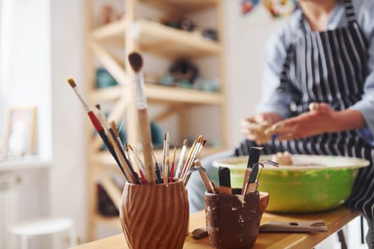 Young female ceramist working by using pottery wheel indoors and making handmade clay product photo