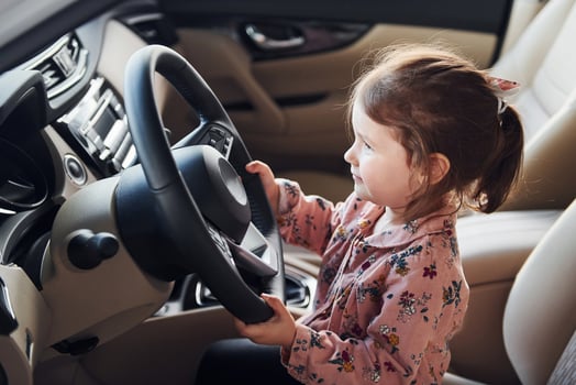 Cute little girl sitting on the driver's seat inside of modern car photo