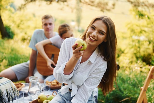 Woman eats apple. Group of young people have vacation outdoors in the forest. Conception of weekend and friendship photo